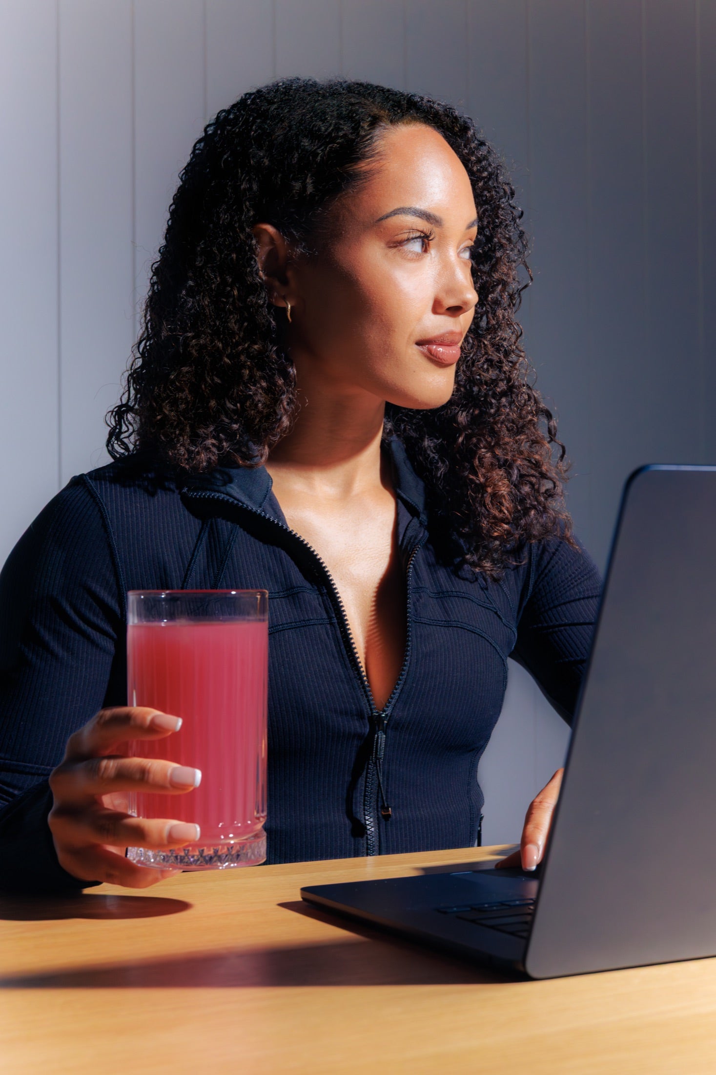 A woman working at a laptop holding a glass of Day Shift