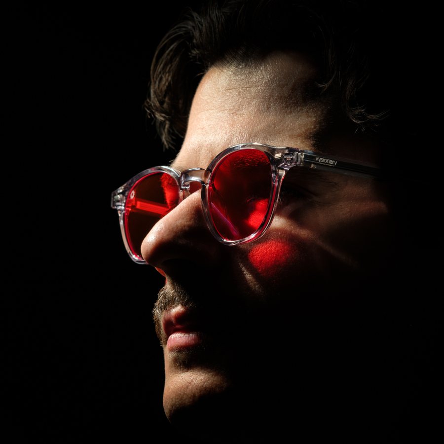 Man in clear-frame red lens glasses in low light